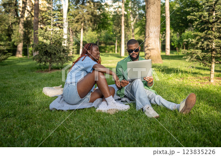 Calm African American couple sits under trees, studying online. Man browses exam resources on gadget 123835226