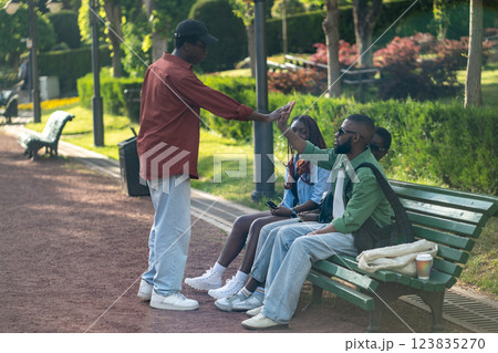 Park gathering, African American students greeting each other with high five, sit on bench together Park gathering, African American students greeting each other with high five, sit on bench together 123835270