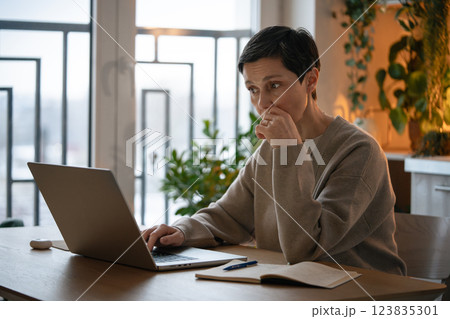 Meeting deadlines. Thoughtful worried mature woman working on laptop, taking notes at home alone 123835301
