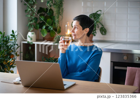 Calm thoughtful mature woman enjoying cup of tea during break from working remotely on laptop Calm thoughtful mature woman enjoying cup of tea during break from working remotely on laptop 123835366