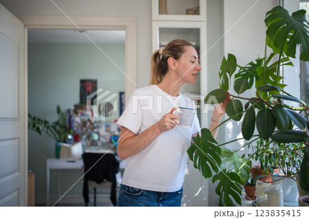 Relaxed woman check, water houseplants in pots, inspecting for ailments or pests. Household chores 123835415