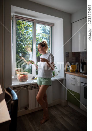 Joyful woman sipping tea, browsing phone on charge in morning kitchen. In touch, check social media Joyful woman sipping tea, browsing phone on charge in morning kitchen. In touch, check social media 123835465
