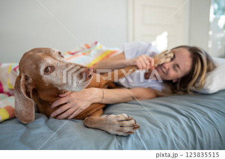 Mischief woman play with dog on bed in morning. Dog put paw on female face, lazy pet before walk 123835515