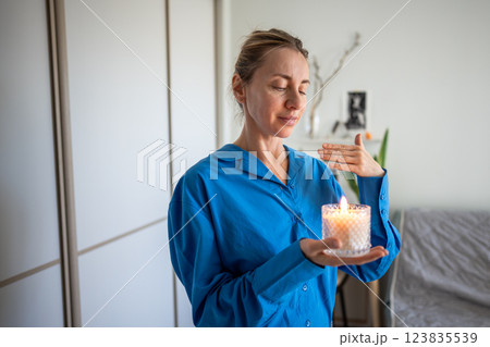 Calm woman enjoy smelling lighted scented candle, meditating, creating cozy atmosphere at home.  123835539