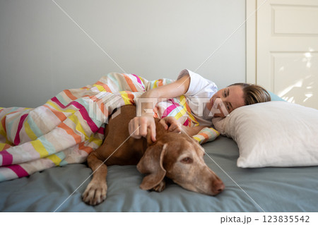 Smiling woman and Magyar Vizsla dog snuggle on bed, enjoying lazy moments at home in morning Smiling woman and Magyar Vizsla dog snuggle on bed, enjoying lazy moments at home in morning 123835542