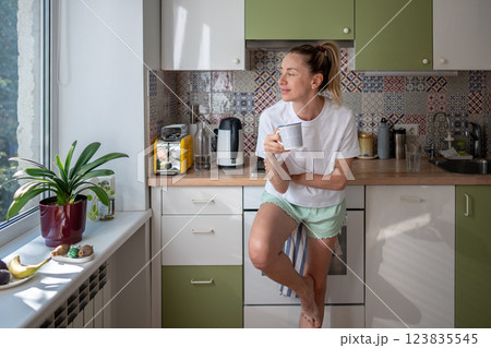 Happy woman enjoy coffee while looking out window in kitchen. No plans, simple living, mindfulness 123835545