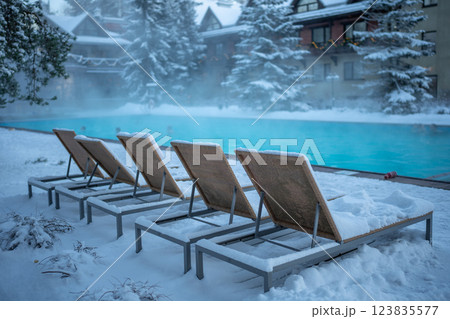 Warm open-air swimming pool with blue water and snow covered loungers in cold weather, outdoor 123835577