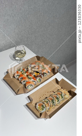 Sushi, rolls, in cardboard boxes. A glass of wine on a white table. 123836330