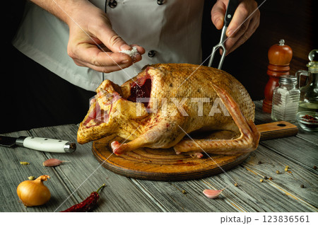 A skilled chef adds salt to a beautifully seasoned duck, preparing it for roasting. The warm kitchen is filled with spices, creating an inviting atmosphere for cooking A skilled chef adds salt to a beautifully seasoned duck, preparing it for roasting. The warm kitchen is filled with spices, creating an inviting atmosphere for cooking 123836561