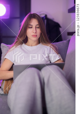 Young woman freelancer working in a white T-shirt comfortably on laptop in modern indoor space during evening hours with warm lighting Young woman freelancer working in a white T-shirt comfortably on laptop in modern indoor space during evening hours with warm lighting 123836673