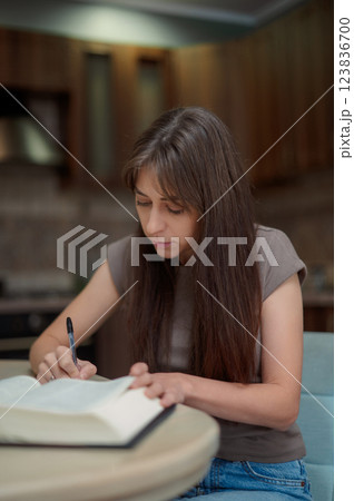 Female student learning and preparing exam at home. Woman reading textbook and taking notes 123836700