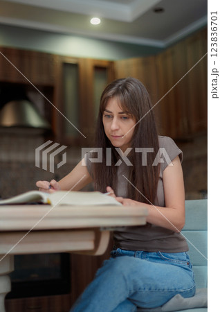 Female student learning and preparing exam at home. Woman reading textbook and taking notes 123836701