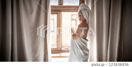 Young woman in a white towel standing by the window in the morning 123836856