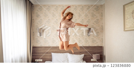 Woman having fun and jumping with bathrobe on bed in hotel room Woman having fun and jumping with bathrobe on bed in hotel room 123836880