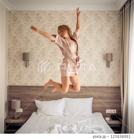 Woman having fun and jumping with bathrobe on bed in hotel room 123836881