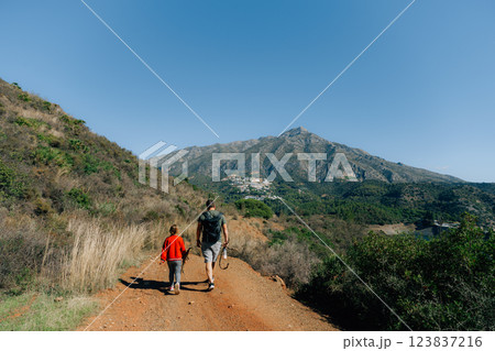 Father and son hiking along mountain trail under clear blue sky Father and son hiking along mountain trail under clear blue sky 123837216