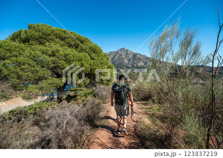 Male hiker walking on mountain trail in sunny mediterranean landscape 123837219