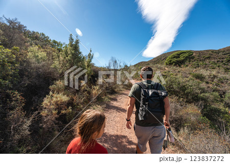 Young adults hiking in nature trail under blue sky with cloud formation Young adults hiking in nature trail under blue sky with cloud formation 123837272