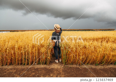 Girl in a wheat field wearing a straw hat on a cloudy day. Back view 123837469