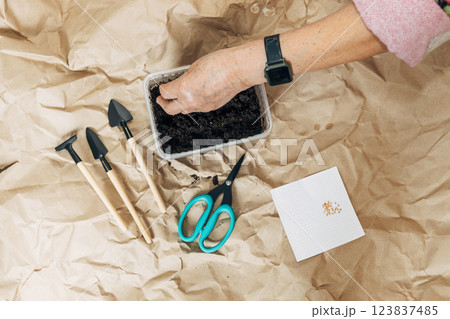 Kraft paper background, fertile soil and garden tools, top view. Hands planting seeds 123837485