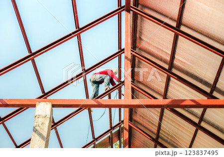 Roofer working in special protective work wear gloves, using air or pneumatic nail gun installing asphalt shingle on top of the new roof, Concept of residential building under construction. Roofer working in special protective work wear gloves, using air or pneumatic nail gun installing asphalt shingle on top of the new roof, Concept of residential building under construction. 123837495