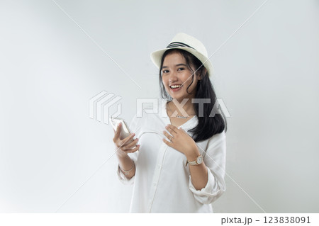 Beautiful young Asian woman tourist in straw hat standing posing with hand holding her smart phone and pointing, woman advertising online purchase 123838091