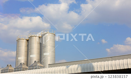 Stainless steel silo amidst blue sky. Warehouse for storing goods and maintaining product quality. Exterior of industrial factory with sky and clouds as background. Stainless steel silo amidst blue sky. Warehouse for storing goods and maintaining product quality. Exterior of industrial factory with sky and clouds as background. 123838157