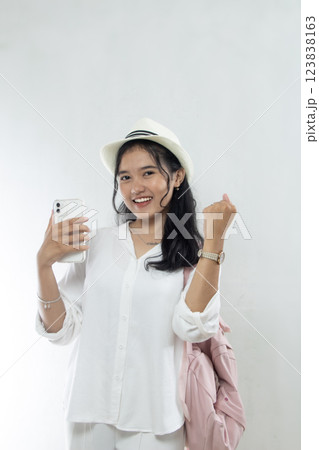 Beautiful young Asian woman tourist in pink straw hat excited and showing smart phone buying tickets online, holiday travel advertising, isolated white background Beautiful young Asian woman tourist in pink straw hat excited and showing smart phone buying tickets online, holiday travel advertising, isolated white background 123838163