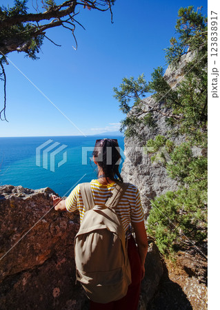 A young female traveler with a backpack sits on the top of Karaul-Oba mountain, Novy Svet village, Crimea, enjoying the sea view. A tourist with a backpack travels through the Crimea, the village of A young female traveler with a backpack sits on the top of Karaul-Oba mountain, Novy Svet village, Crimea, enjoying the sea view. A tourist with a backpack travels through the Crimea, the village of 123838917