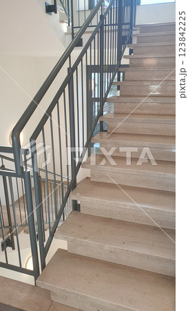 Internal staircase with marble stone beige stairs inside the building and metal railings. Internal staircase with marble stone beige stairs inside the building and metal railings. 123842225