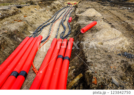 Laying new underground high-voltage power cable in red corrugated protective tube 123842750