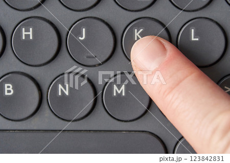 Close up of finger pressing k key on black keyboard with circular buttons Close up of finger pressing k key on black keyboard with circular buttons 123842831