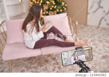 A woman is comfortably sitting on a pink couch while reading a book A woman is comfortably sitting on a pink couch while reading a book 123842883