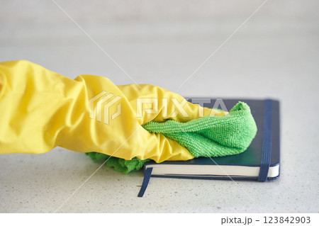 Gloved hand cleaning book with green cloth on light gray surface for hygienic 123842903