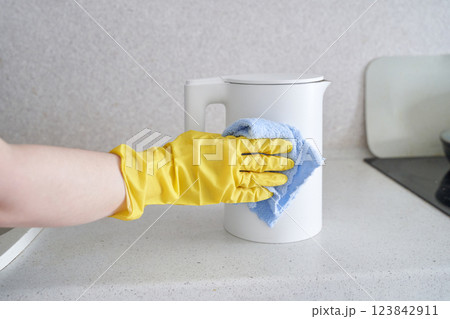 Cleaning white electric kettle with yellow glove and blue cloth on kitchen count 123842911
