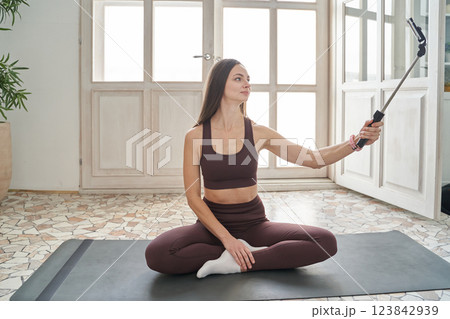 A woman is sitting on her yoga mat and is happily taking a selfie A woman is sitting on her yoga mat and is happily taking a selfie 123842939