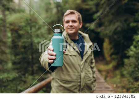 Happy blonde man in sport clothes having a halt after hiking. 30s Hiker drinking water from water bottle or hot drink from blue thermos. Travel, adventure, active lifestyle. High quality photo. Happy blonde man in sport clothes having a halt after hiking. 30s Hiker drinking water from water bottle or hot drink from blue thermos. Travel, adventure, active lifestyle. High quality photo. 123843502