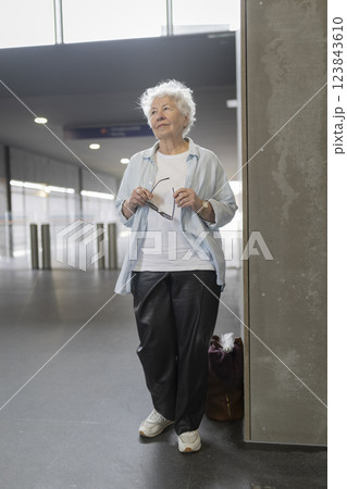 Senior woman waiting in airport terminal holding eyeglasses Senior woman waiting in airport terminal holding eyeglasses 123843610