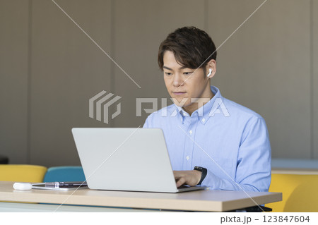 イヤホンをしてノートパソコンに向かう30代のビジネスマン 123847604