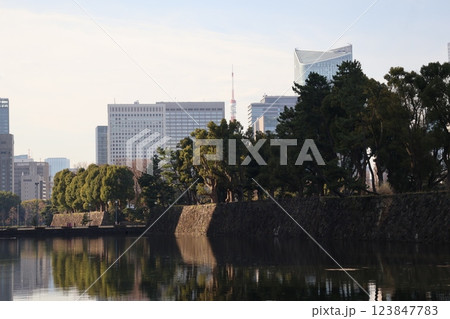 白い雲と青空と高層ビルの街並みと皇居の石垣と緑の樹々の森などが濠の水面にうつる風景 123847783