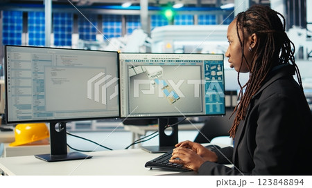 Programmer in photovoltaics factory using PC to update software of robot arms placing solar panels on assembly lines. Woman coding on computer, upgrading solar plant machinery, camera A Programmer in photovoltaics factory using PC to update software of robot arms placing solar panels on assembly lines. Woman coding on computer, upgrading solar plant machinery, camera A 123848894