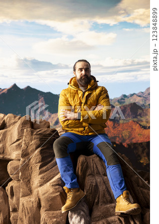 Male trekker takes in the breathtaking mountain landscape on rocks, enjoying the scenic background, crisp air and rugged peaks. Excitement of discovering new horizons for wellbeing. 123848899