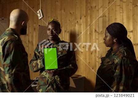 Team of military units at shooting range watching video on green screen tablet to learn necessary combat skills. Army soldiers looking at instructions on chroma key device during training 123849021