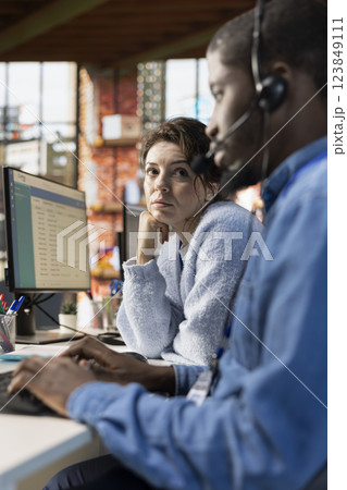 Call center agents collaborating, logging customer interactions in spreadsheet document on computer. Customer service agent and african american coworker using customer service management software 123849111