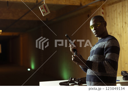 Portrait of shooting range customer reloading pistol, preparing to shoot targets, having fun. Man at indoor shooting ground facility loading pistol, wearing protection goggles Portrait of shooting range customer reloading pistol, preparing to shoot targets, having fun. Man at indoor shooting ground facility loading pistol, wearing protection goggles 123849134