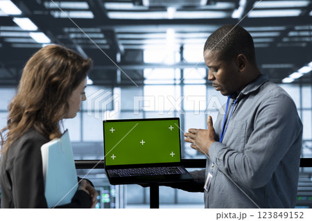 Engineers in data center using isolated screen notebook, observing analytics, reviewing equipment health. Workers using mockup laptop, adjusting system parameters, doing maintenance tasks Engineers in data center using isolated screen notebook, observing analytics, reviewing equipment health. Workers using mockup laptop, adjusting system parameters, doing maintenance tasks 123849152
