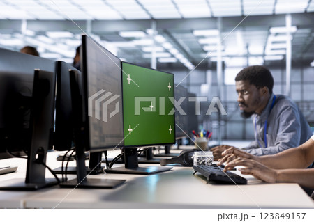 Engineer in server hub ensuring data remains shielded from potential threats using green screen PC. Employee safeguarding data center hardware against malicious access with mockup computer display 123849157