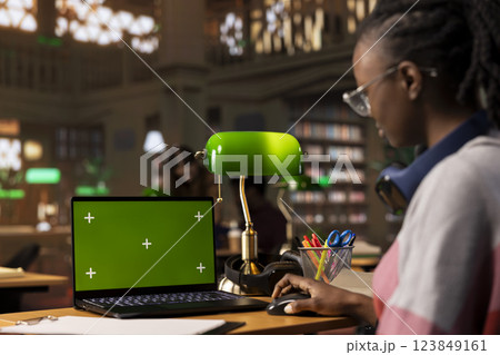 University student collecting notes from academic sources next to green screen, using the library database and books collection for scientific research. Young adult working on bachelor paper. 123849161