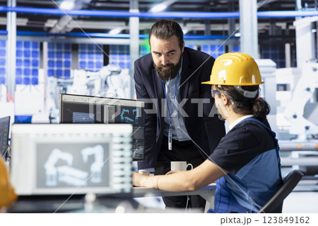 Solar panels plant manager giving feedback to employee on optimizing efficiency after analyzing data. Photovoltaics factory supervisor overseeing man working on innovative solar cells design prototype Solar panels plant manager giving feedback to employee on optimizing efficiency after analyzing data. Photovoltaics factory supervisor overseeing man working on innovative solar cells design prototype 123849162