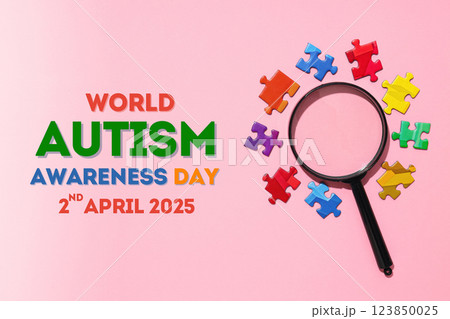 Autism Day, magnifying glass and colorful puzzles on a pink background, with text, top view 123850025